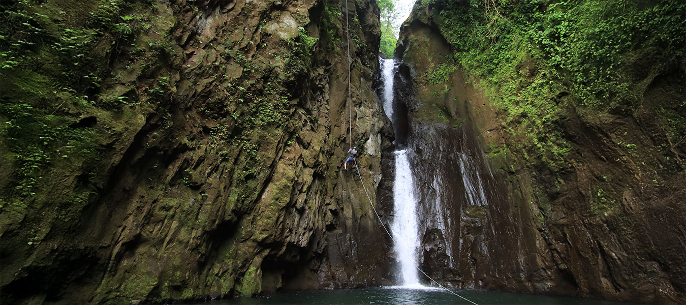 Adventurer rappelling down a tall rainforest waterfall during the Rainforest Falls canyoning experience in La Fortuna, Costa Rica.