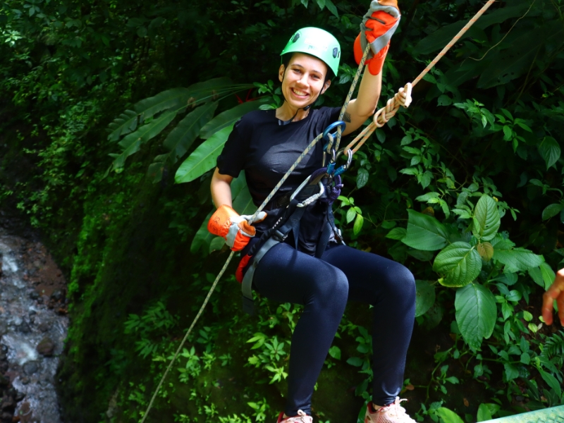 Woman smiling while waterfall rappelling during Pure Trek Canyoning adventure in La Fortuna, Costa Rica rainforest