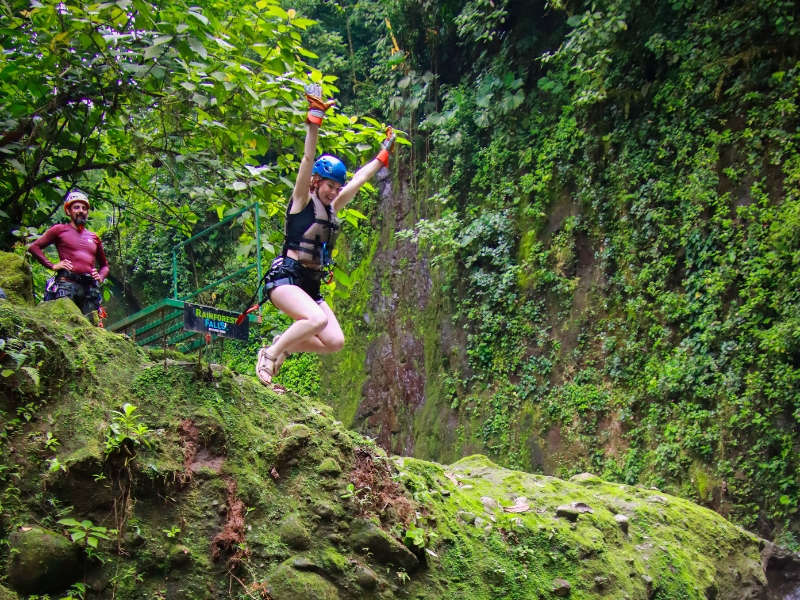 Woman jumping into a rainforest pool during the Rainforest Falls canyoning adventure near La Fortuna, Costa Rica.