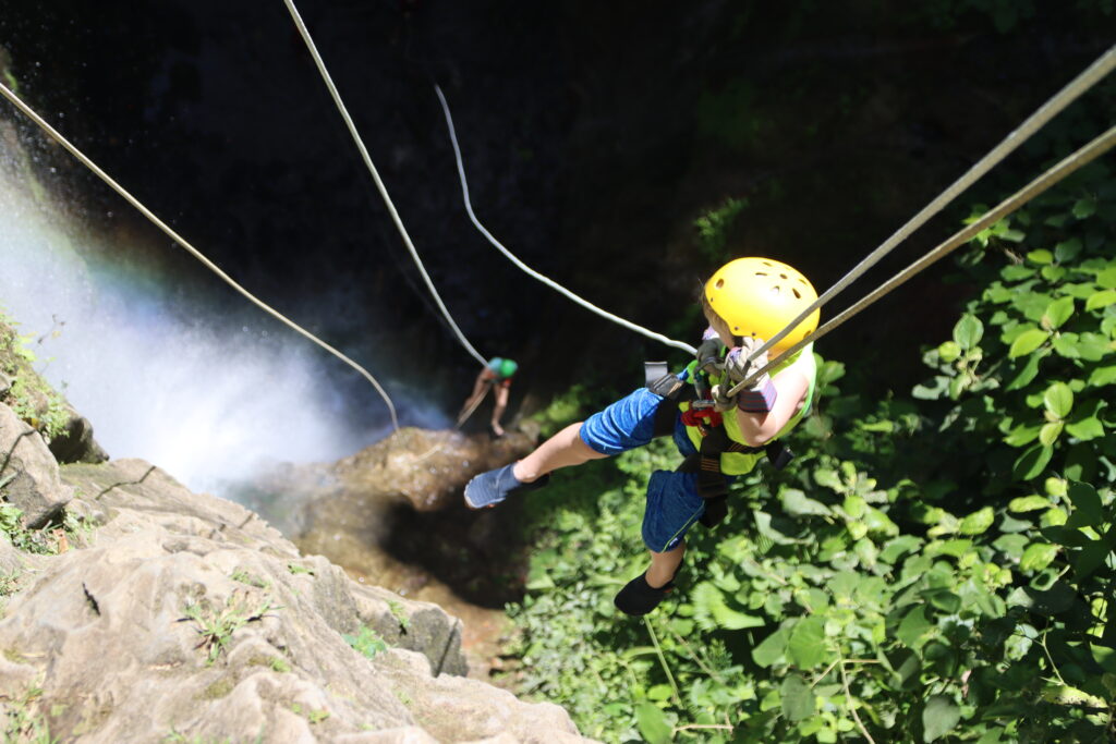 Child descending a waterfall during a guided canyoning experience with Pure Trek in La Fortuna, Costa Rica.