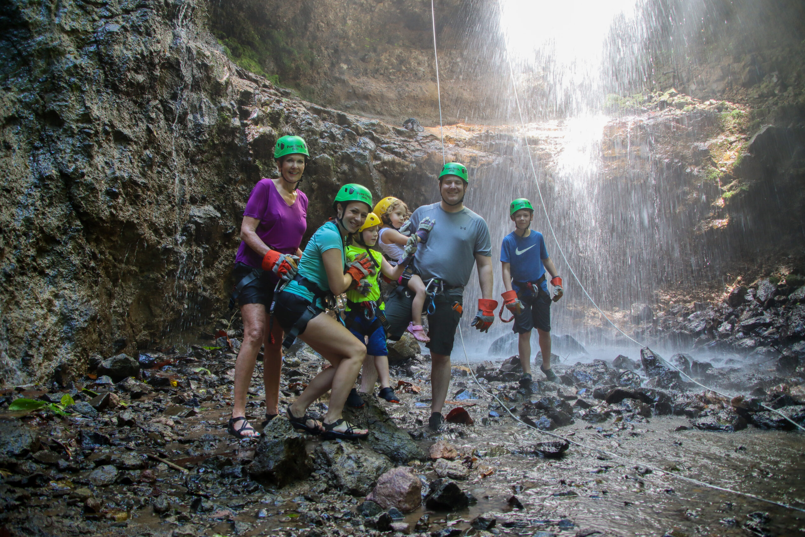 Family enjoying a guided canyoning adventure beneath a waterfall with Pure Trek in La Fortuna, Costa Rica.