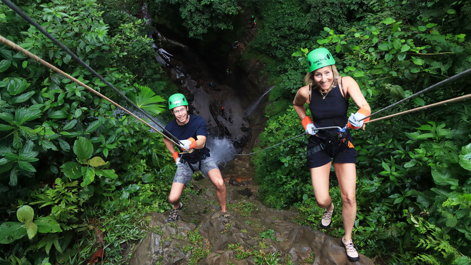 Two adventurers rappelling down a rainforest canyon during a Pure Trek canyoning tour in La Fortuna, Costa Rica.