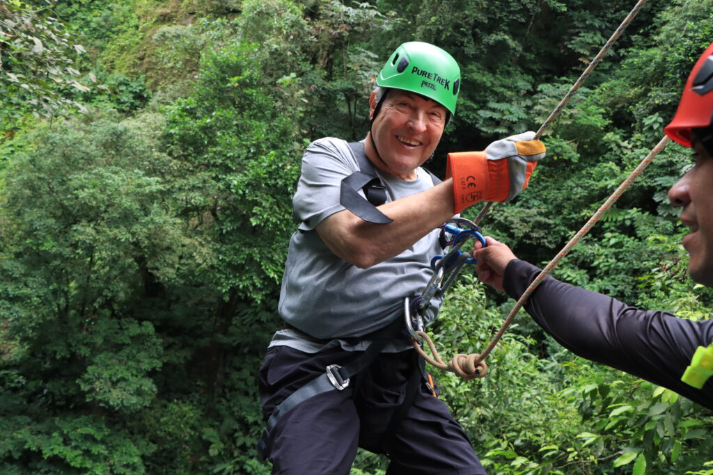 Smiling guest rappelling with professional guide assistance during a Pure Trek canyoning tour in La Fortuna, Costa Rica.