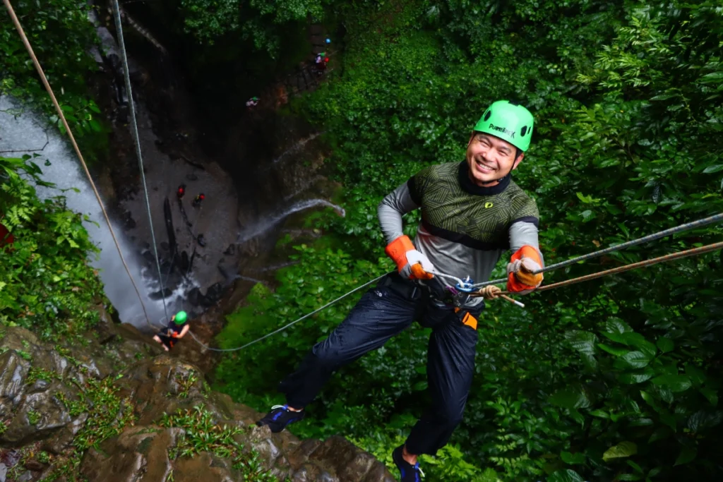 Guest smiling while rappelling down a jungle waterfall during the green season adventure in Arenal, Costa Rica.